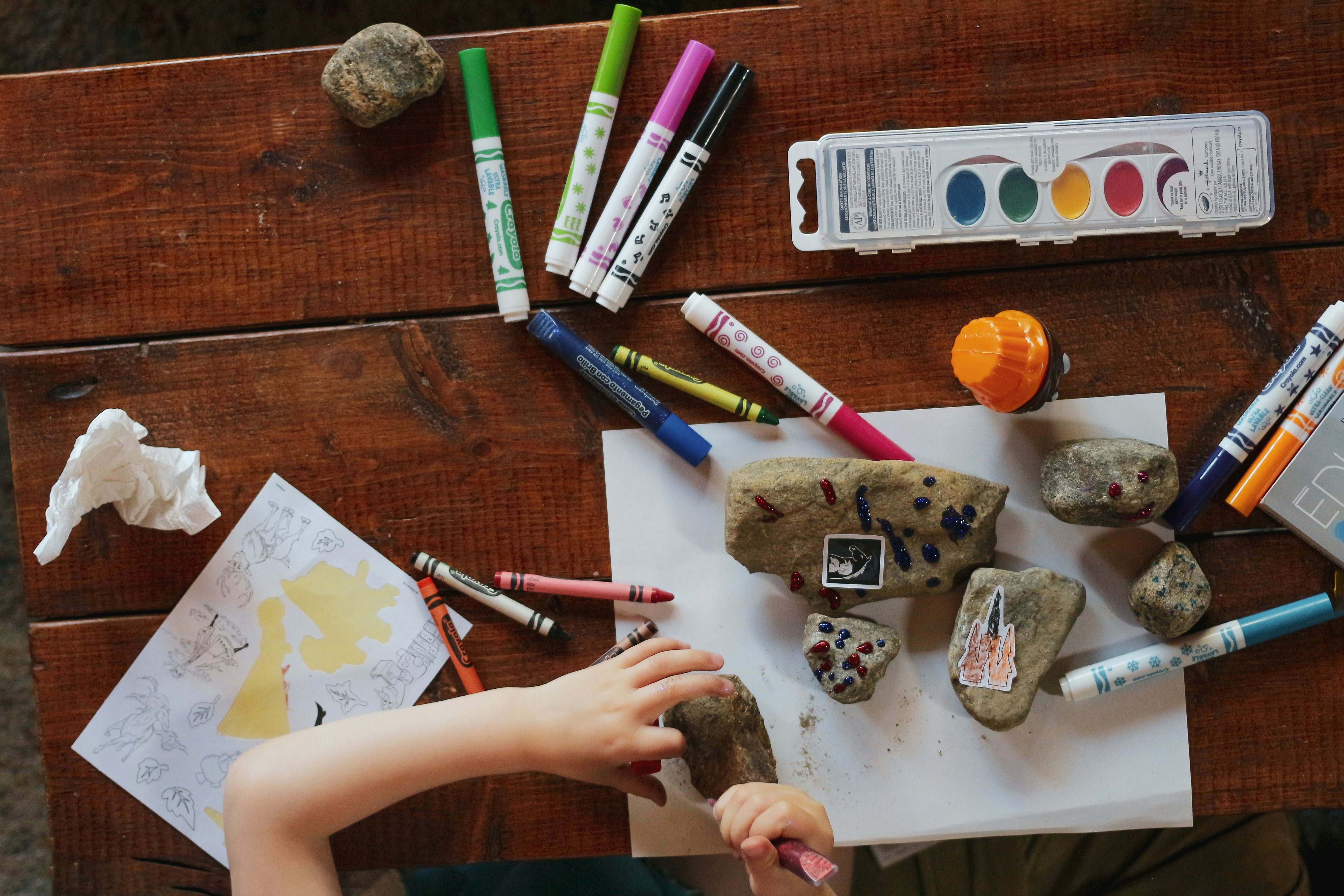 Kind bastelt am Gartentisch aus Holz mit Steinen, Farben und Papier    Credit: sigmund-OV44gxH71DU-unsplash